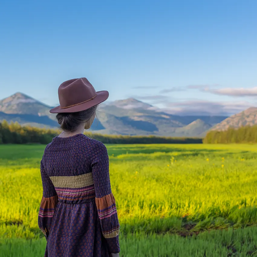 mujer con sombrero de espaldas mirando un campo verdoso